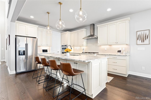 kitchen with dark wood finished floors, an island with sink, stainless steel appliances, wall chimney range hood, and tasteful backsplash