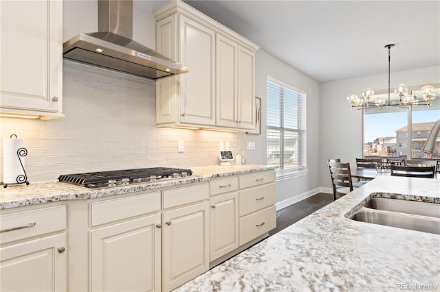 kitchen with light stone counters, baseboards, stainless steel gas cooktop, wall chimney exhaust hood, and tasteful backsplash