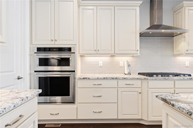 kitchen with stainless steel appliances, wall chimney exhaust hood, decorative backsplash, and white cabinetry