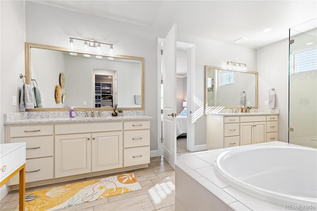 bathroom with a bath, a spacious closet, two vanities, and a sink