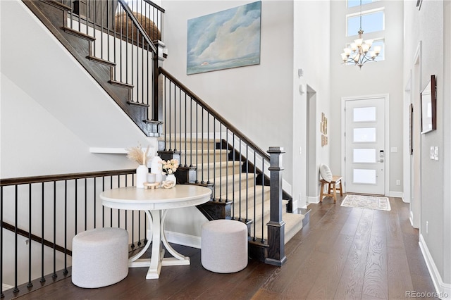 foyer entrance with wood-type flooring, a chandelier, baseboards, a towering ceiling, and stairs