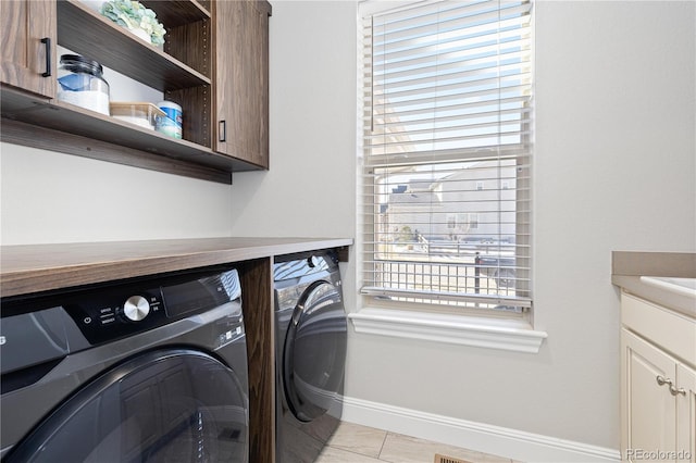 clothes washing area with light tile patterned floors, cabinet space, baseboards, and washer and clothes dryer