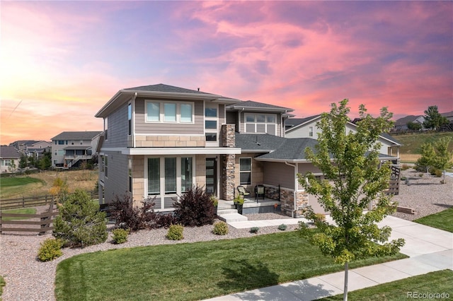 prairie-style home featuring fence, covered porch, concrete driveway, a garage, and stone siding