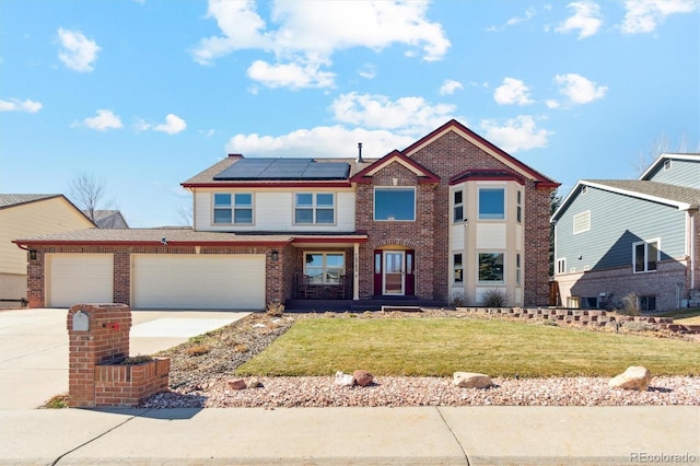 traditional-style home with brick siding, concrete driveway, a front yard, roof mounted solar panels, and a garage