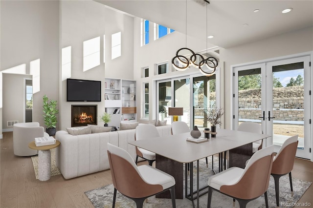 dining room featuring a warm lit fireplace, visible vents, wood finished floors, french doors, and recessed lighting