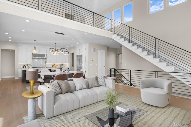 living room featuring recessed lighting, visible vents, a towering ceiling, light wood-style floors, and stairs