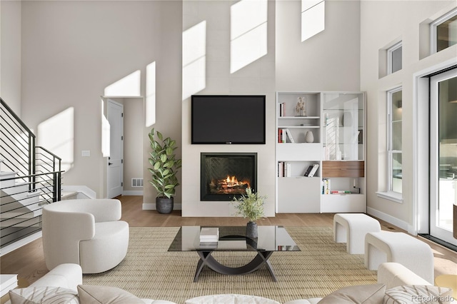 living area with visible vents, a fireplace, a towering ceiling, and wood finished floors