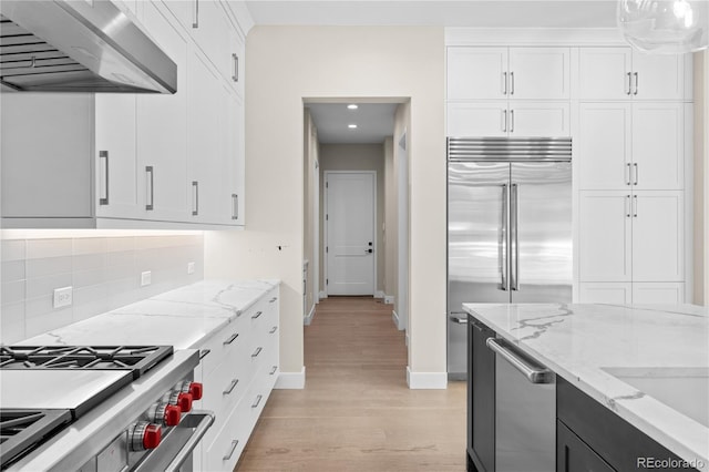 kitchen featuring range hood, backsplash, light wood-style floors, white cabinetry, and high quality appliances