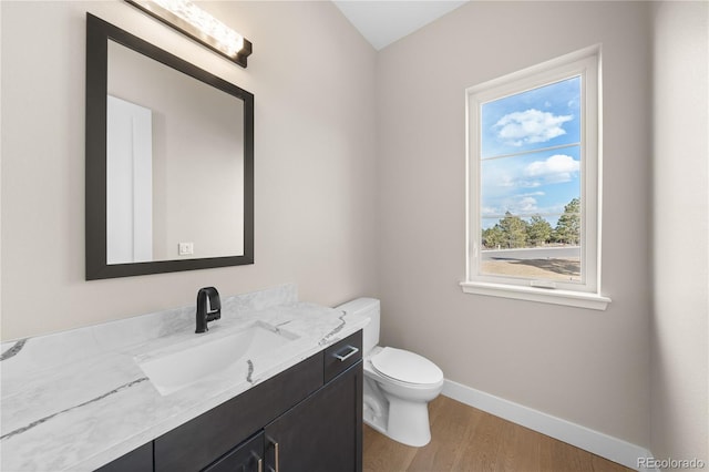 half bathroom with toilet, wood finished floors, vanity, and baseboards