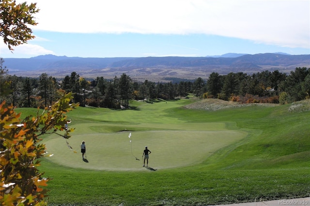 view of community with view of golf course, a mountain view, and a lawn