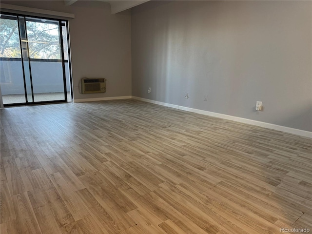 empty room featuring light wood-type flooring, baseboards, and a wall mounted AC