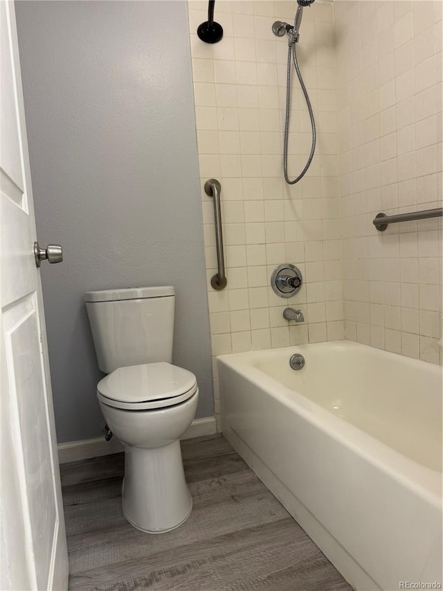 full bath featuring washtub / shower combination, wood finished floors, toilet, and baseboards