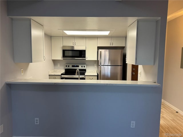 kitchen featuring light wood finished floors, light countertops, appliances with stainless steel finishes, and baseboards