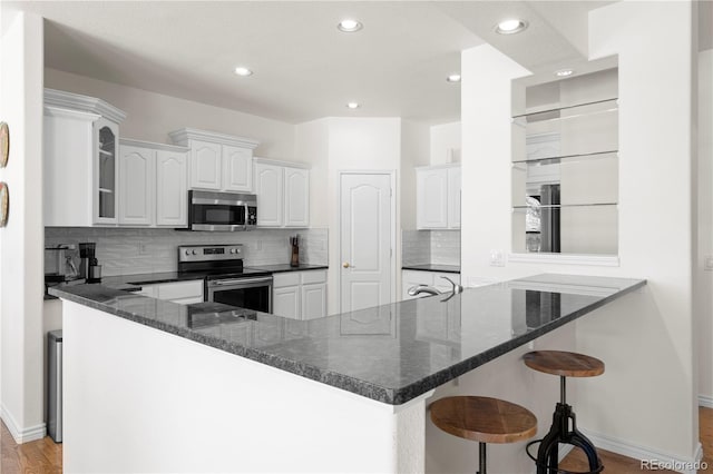 kitchen with a kitchen breakfast bar, kitchen peninsula, white cabinetry, and appliances with stainless steel finishes