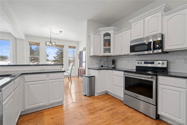 kitchen with backsplash, white cabinets, light hardwood / wood-style flooring, stainless steel appliances, and a chandelier