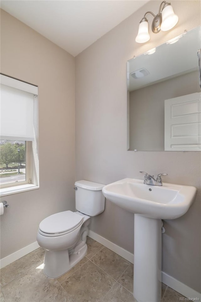 half bathroom featuring toilet, baseboards, and a sink