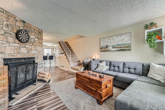 living area with a textured ceiling, wood finished floors, stairway, and a fireplace