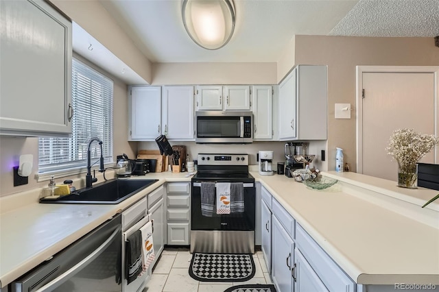 kitchen featuring appliances with stainless steel finishes, a sink, light countertops, light tile patterned floors, and a peninsula