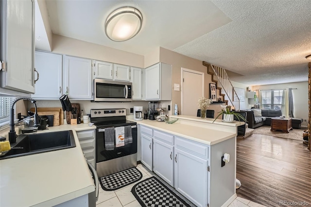 kitchen with stainless steel appliances, open floor plan, a sink, a peninsula, and light countertops