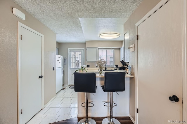 kitchen with freestanding refrigerator, a textured ceiling, a peninsula, a breakfast bar, and light countertops