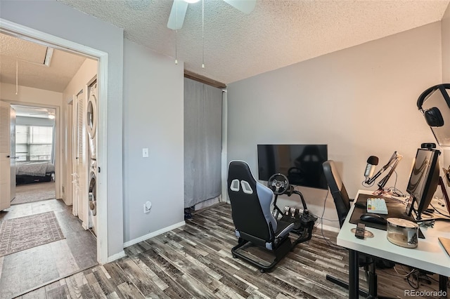 office area featuring stacked washer and clothes dryer, wood finished floors, a textured ceiling, attic access, and ceiling fan