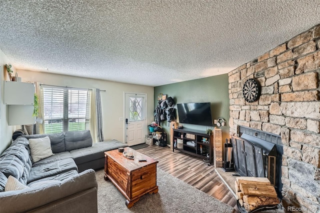 living area with a textured ceiling, wood finished floors, and a stone fireplace