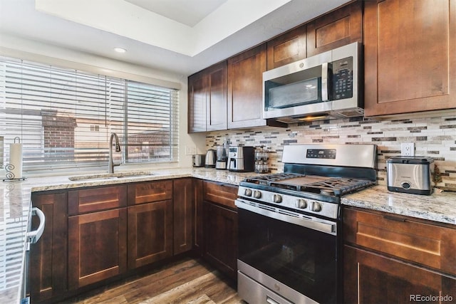 kitchen featuring light stone counters, wood finished floors, a sink, stainless steel appliances, and tasteful backsplash