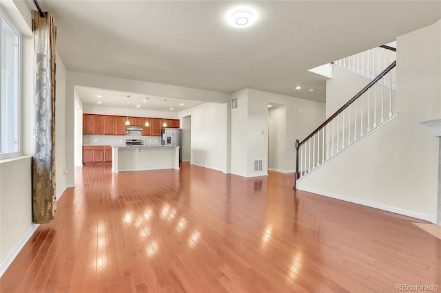 unfurnished living room with visible vents, stairs, light wood-style floors, and baseboards