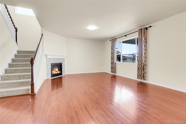 unfurnished living room featuring a fireplace, baseboards, wood-type flooring, and stairs