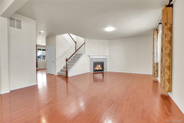 unfurnished living room featuring visible vents, light wood-style floors, stairway, and a tile fireplace