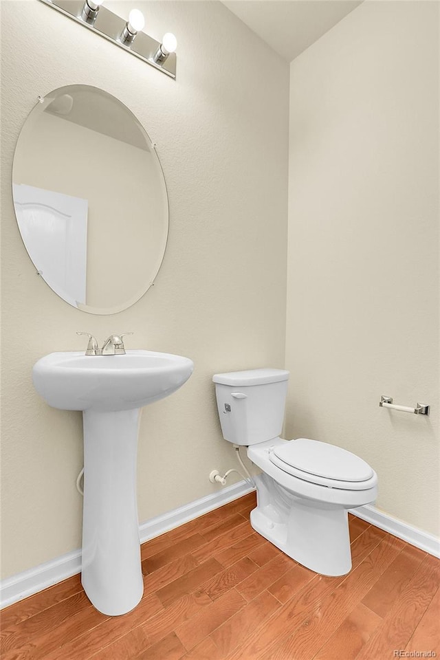 bathroom featuring toilet, baseboards, a sink, and wood finished floors