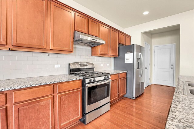 kitchen featuring decorative backsplash, brown cabinets, light wood finished floors, under cabinet range hood, and stainless steel appliances