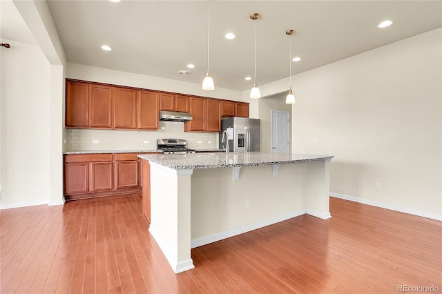 kitchen with under cabinet range hood, stainless steel appliances, brown cabinetry, and decorative backsplash