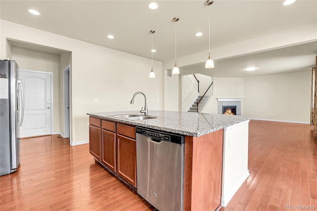 kitchen with a sink, a center island with sink, stainless steel appliances, and light wood finished floors