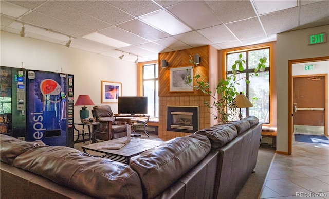 living room with tile patterned floors, rail lighting, a paneled ceiling, wooden walls, and a fireplace