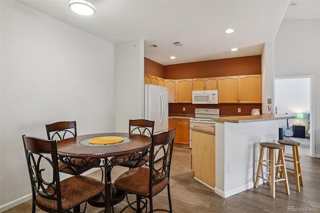 9692 W Coco Cir Unit 304, Littleton, CO 80128 - kitchen with white appliances, dark wood finished floors, light brown cabinets, a peninsula, and a kitchen breakfast bar