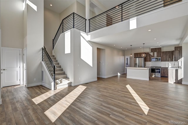 unfurnished living room with wood-type flooring, a towering ceiling, and sink