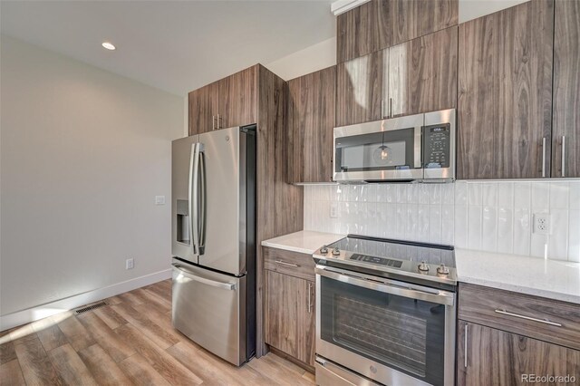 kitchen with tasteful backsplash, light stone counters, stainless steel appliances, and light wood-type flooring