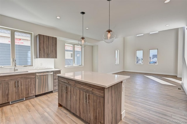 kitchen with pendant lighting, dishwasher, a center island, sink, and light hardwood / wood-style floors