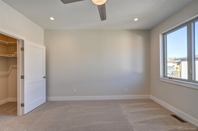 unfurnished bedroom featuring a spacious closet, a closet, ceiling fan, and light carpet