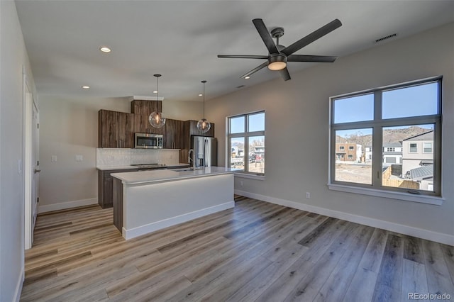 kitchen with appliances with stainless steel finishes, sink, a center island with sink, decorative light fixtures, and light hardwood / wood-style floors