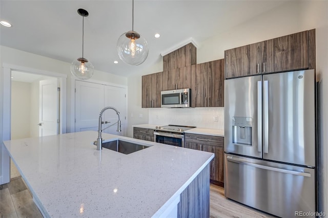 kitchen with a kitchen island with sink, light stone countertops, sink, and appliances with stainless steel finishes