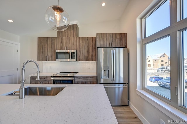 kitchen featuring sink, hanging light fixtures, light hardwood / wood-style flooring, light stone countertops, and stainless steel appliances