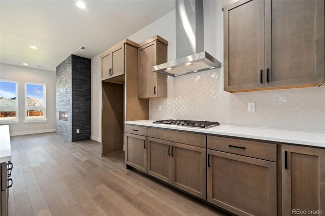 1724 Barefoot Dr, Windsor, CO 80550 - kitchen featuring wall chimney range hood, stainless steel gas stovetop, light wood-style flooring, tasteful backsplash, and light countertops