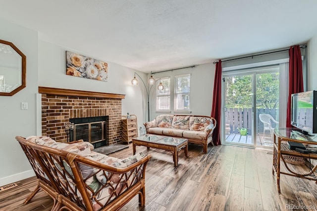 living room with a brick fireplace, wood finished floors, visible vents, and baseboards