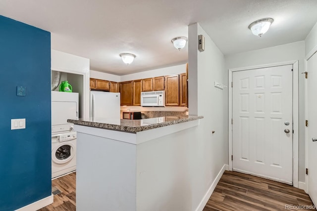 kitchen featuring dark wood-type flooring, white appliances, brown cabinetry, and stacked washer and clothes dryer