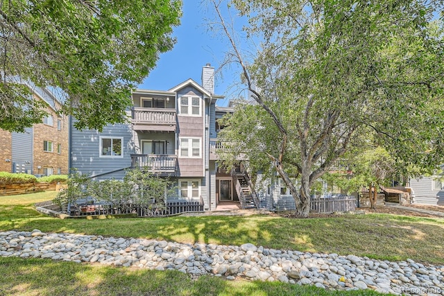 view of front of house featuring a chimney, stairway, a front yard, fence, and a balcony