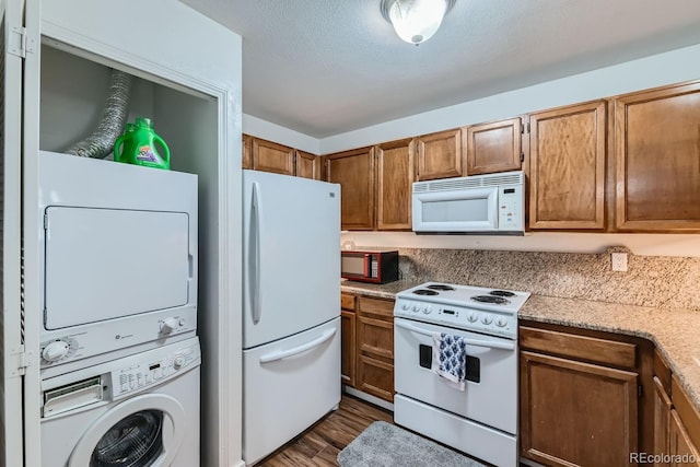 kitchen featuring brown cabinetry, white appliances, dark wood-type flooring, and stacked washing maching and dryer