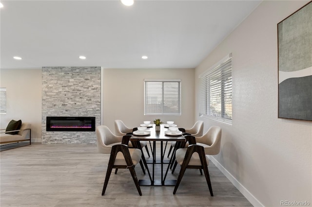 dining room with light wood finished floors, a stone fireplace, recessed lighting, and baseboards