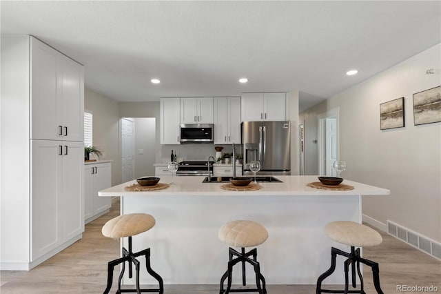 kitchen with a breakfast bar area, a kitchen island with sink, stainless steel appliances, visible vents, and light countertops